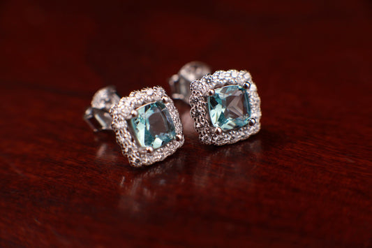 May include: A pair of silver earrings with a square-shaped blue gemstone surrounded by smaller clear gemstones.
